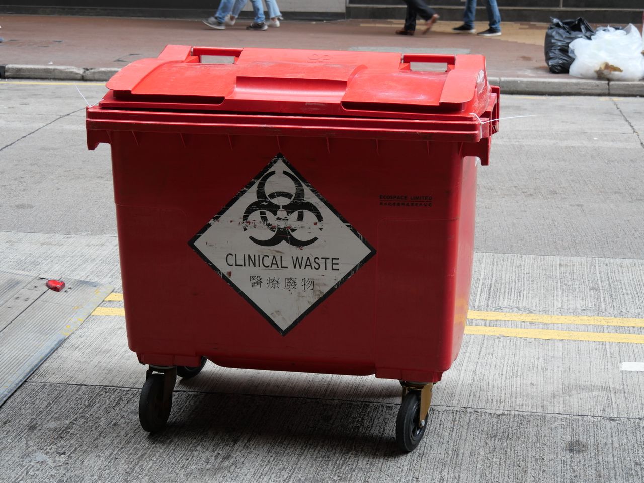 A red wheeled bin labeled for clinical waste management on a city street.